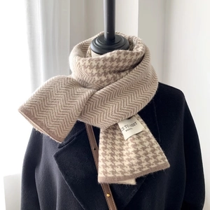 Close-up of a camel houndstooth knitted scarf paired with a black wool coat on a mannequin