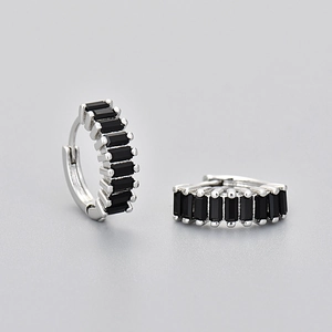 Macro detail of silver rectangular earrings with black baguette-cut zircons on gray background