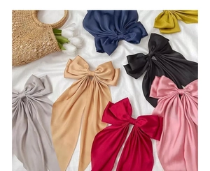 Flat lay of satin bow hair clips in multiple colors on a soft white fabric background