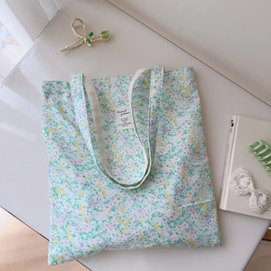 Flat lay detail of a floral cotton tote bag with a white woven label and soft pastel print
