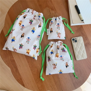 Three sizes of cotton drawstring bags with bear prints and green ribbons on wooden table