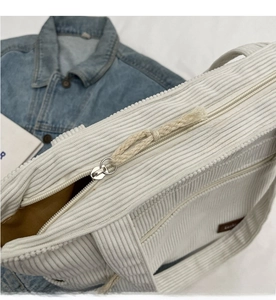 Detail of smooth metal zipper and textured white corduroy fabric on a tote bag