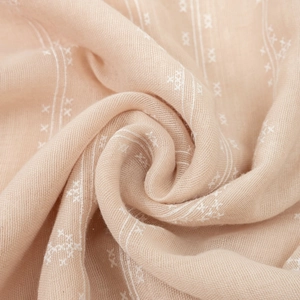 Close-up of beige cotton linen shawl with delicate white star embroidery texture