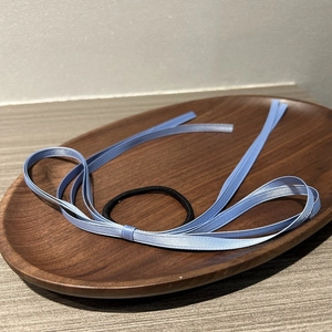 Detail view of a black elastic hair tie with a blue satin ribbon bow on a wooden tray