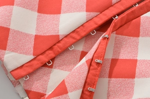 Macro shot of metal hook-and-eye closures on red and white plaid halter top fabric