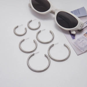 Three pairs of minimalist polished stainless steel hoop earrings in varying sizes on white backdrop
