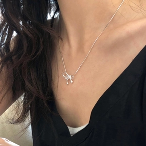 Detail of elegant silver bow pendant necklace worn by model on a sleek snake chain