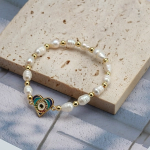 Detailed macro view of heart-shaped evil eye charm and freshwater pearls on golden bracelet