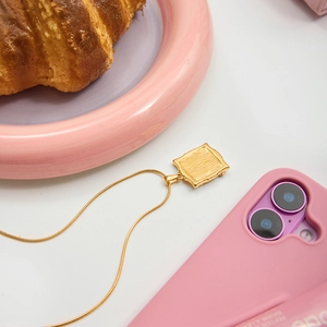 Detail of a square gold pendant with linear texture on a fine chain with stylish props