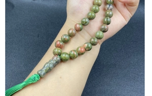 Detail shot of natural unakite prayer beads with green tassel on a person's hand