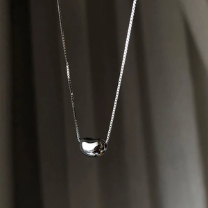 Polished bean pendant on a silver box chain over elegant draped fabric background
