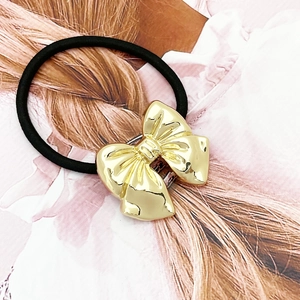 Elastic black hair tie with a textured gold bow charm shown on a stylish display card