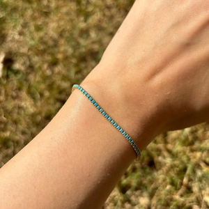 Close-up of a gold chain bracelet with green cubic zirconia stones on a woman's wrist