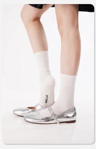 Details von weißen Strick-Crew-Socken mit HELLO-Logo und silbernen Mary Jane Schuhen