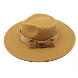 Detail view of the camel wool fedora hat featuring a satin ribbon bow and metal M logo
