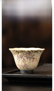 Detail of hand-painted wisteria on a white ceramic teacup with elegant scalloped rim