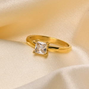 Detail of gold-plated ring featuring a square-cut clear zircon on champagne silk background