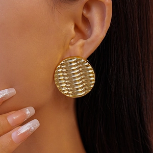 Close-up of golden wavy textured circular stud earring worn by model in professional lighting