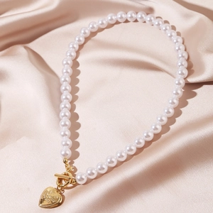 Detailed view of a baroque pearl necklace with a gold heart pendant on champagne silk