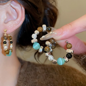 Close-up of bohemian C-shaped hoop earrings with tiger eye stones and pearls