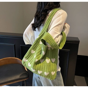 Bolso tote de punto verde con corazones blancos, llevado al hombro en ambiente casual
