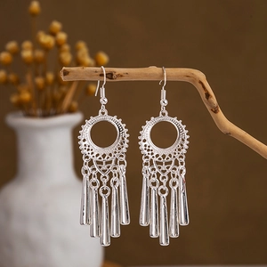 Detailed close-up of ethnic silver tassel earrings with peacock bells on a wooden branch