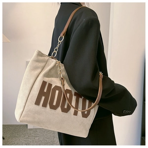 Detail of large tote bag in beige canvas with leather straps and metal chain link decoration