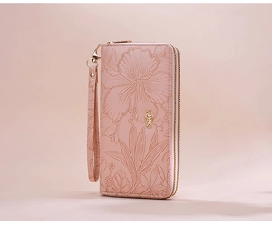Detail of light pink leather wallet featuring 3D floral embossing and double zippers