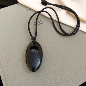 Detail of minimalist black oval geometric pendant on a black leather cord over a book