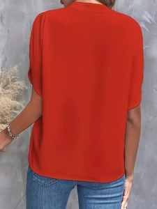 Back view of a casual loose red V-neck shirt paired with denim jeans on a gray background