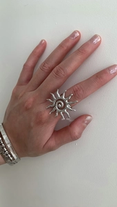 Macro detail of exaggerated silver sun ring with textured wrinkles and hollow design