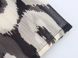 Detail of bohemian chiffon dress fabric with black ink print and gold thread weaves