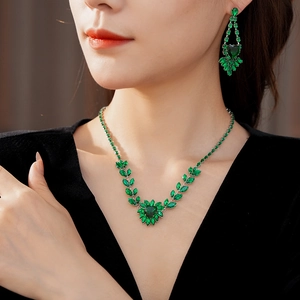 Detailed view of necklace and earrings with green stones and leaf pattern on model