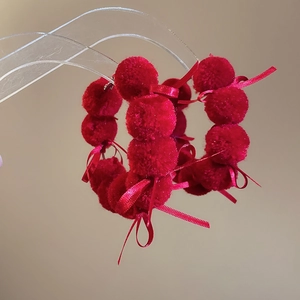Macro shot of red plush ball earrings with a ribbon bow on a clear acrylic stand
