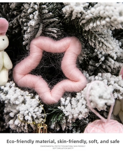 Detail of handcrafted pink star and white rabbit yarn ornaments on snowy pine branches