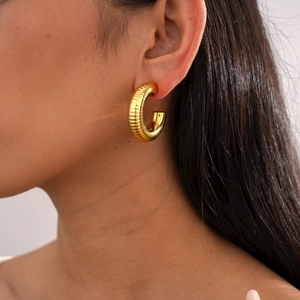 Close-up of golden C-shaped earrings with spiral texture worn by a model