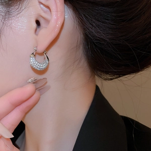 Macro side view of a model wearing sparkling round zircon huggie earrings in silver finish