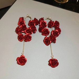 Detail of red rose tassel earrings with gold chain and pearl on grey leather background