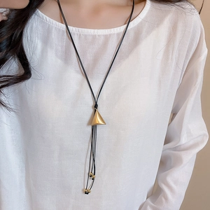 Detailed view of a gold triangular pendant on a black cord worn over a white linen shirt