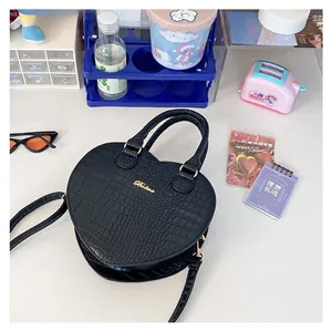 Détail du sac à main noir en forme de cœur avec texture crocodile et logo Balina