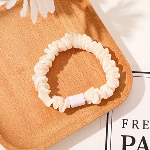 Close-up of a cream pleated satin scrunchie with a rectangular buckle on a wooden tray