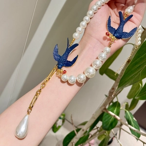 Close-up of vintage bird necklace with blue lacquer swallow and teardrop pearl pendant