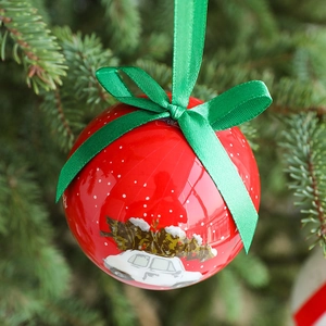 Red Christmas ball ornament with green ribbon bow hanging on a green pine tree