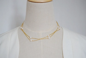Detail of layered gold chain necklace featuring delicate white freshwater pearls
