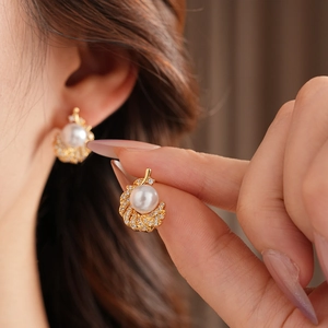 Close-up of elegant gold feather earrings with white pearls and sparkling cubic zirconia