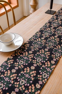 Close-up of black woven table runner with pink floral jacquard on light wood dining table