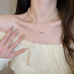 Detail of layered gold choker with faux pearls and curved metal tube pendant on neck