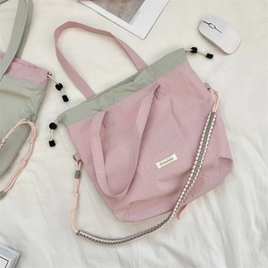 Flat lay of a pink and green canvas tote bag with side drawstrings and woven strap