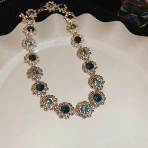 Detailed view of silver flower necklace links with blue crystals on a white ceramic plate
