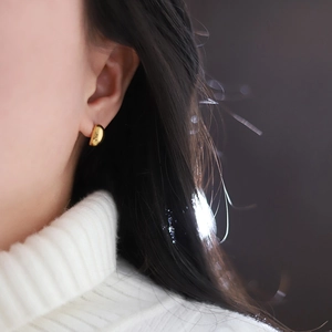 Detail showing high-polish golden dome earrings on ear with elegant metallic luster